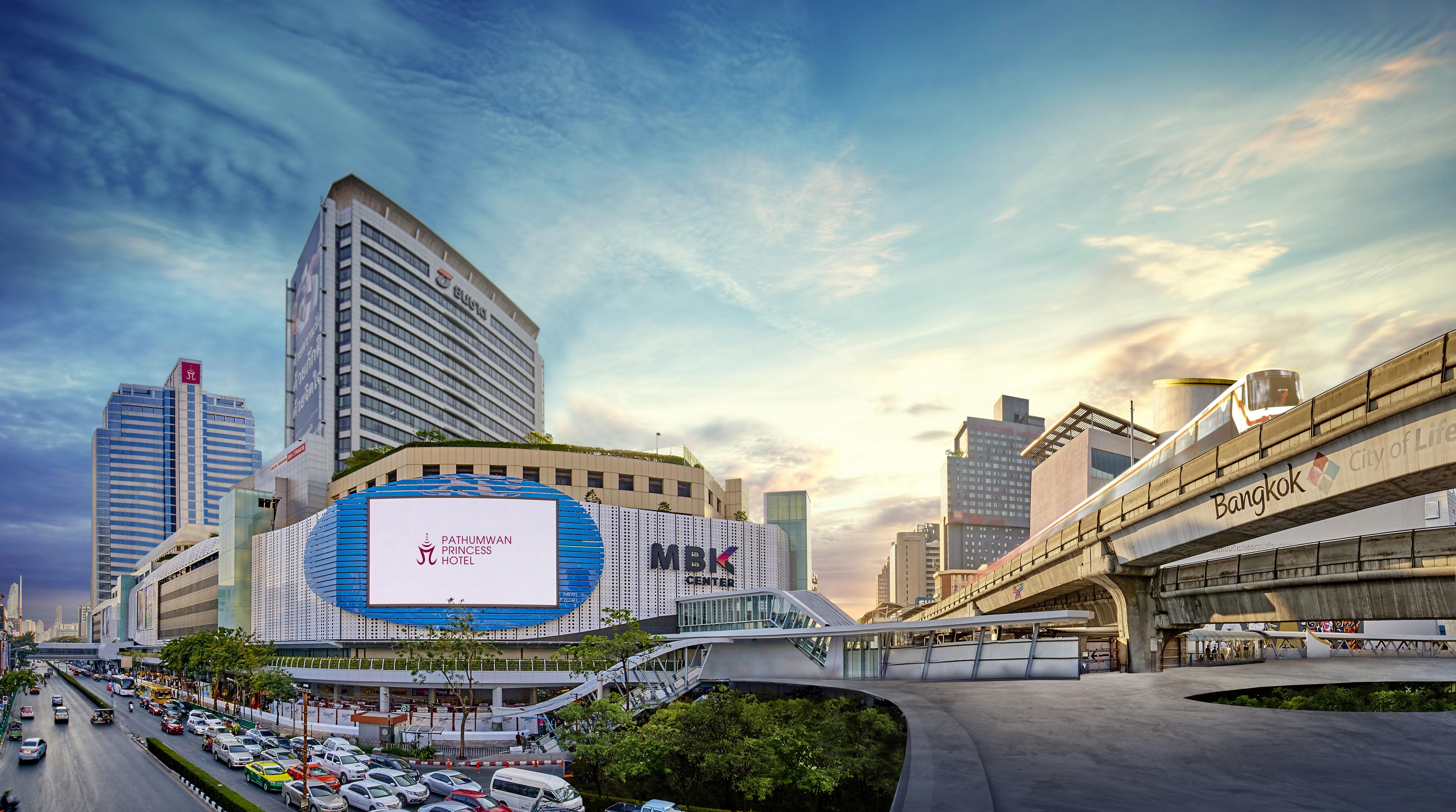 Pathumwan Princess Hotel - Sha Extra Plus Certified Bangkok Exterior foto The photo shows a modern commercial complex, likely a shopping mall, identified as MBK Center, situated in an urban environment. The building features a large digital billboard displaying advertisements. In the foreground, there are cars parked and a