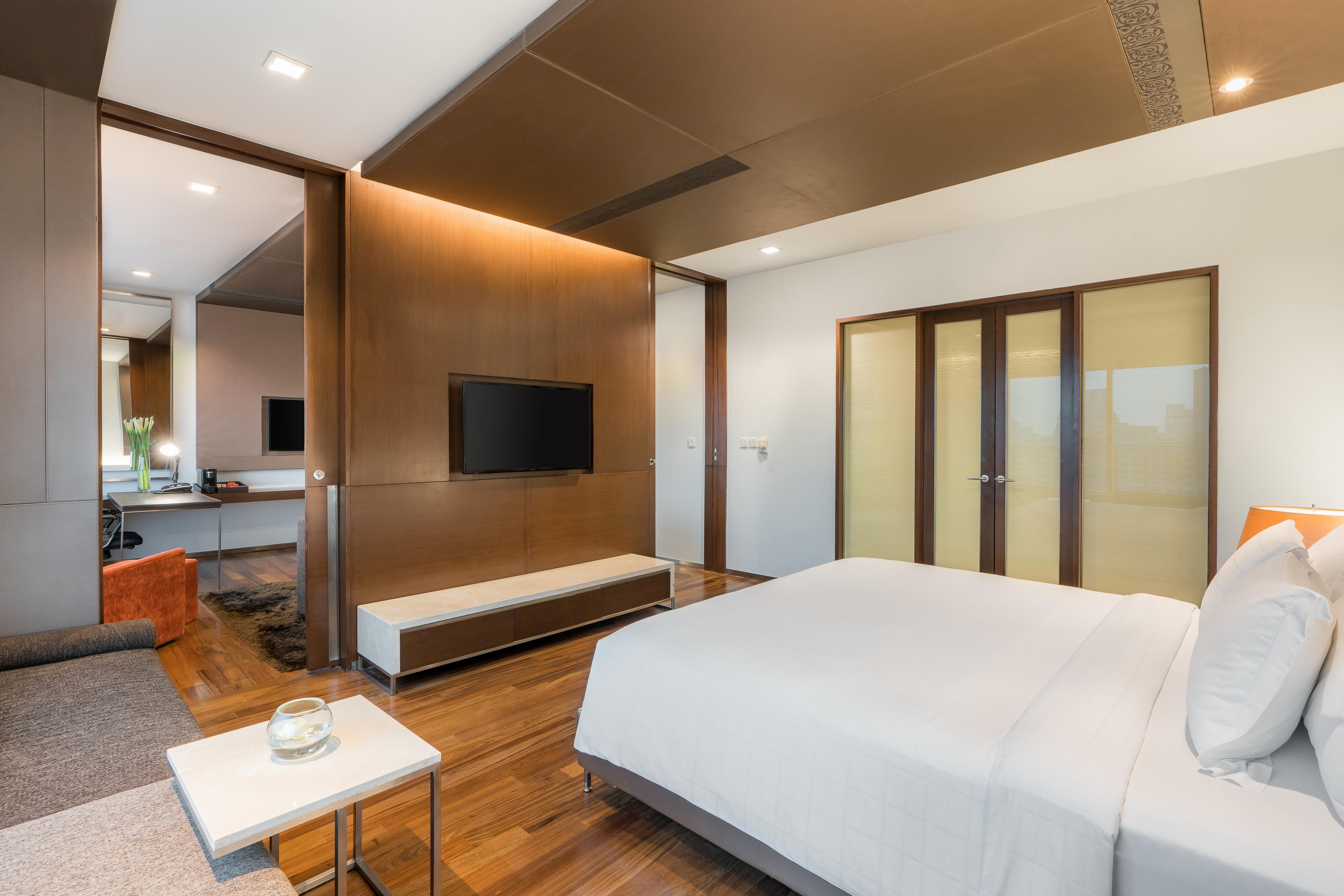 Pathumwan Princess Hotel - Sha Extra Plus Certified Bangkok Exterior foto The photo shows a modern and stylish bedroom. It features a comfortable bed with white bedding, a sleek wooden floor, and a minimalistic design. There's a large television mounted on the wall opposite the bed. In the background, there are glass doors
