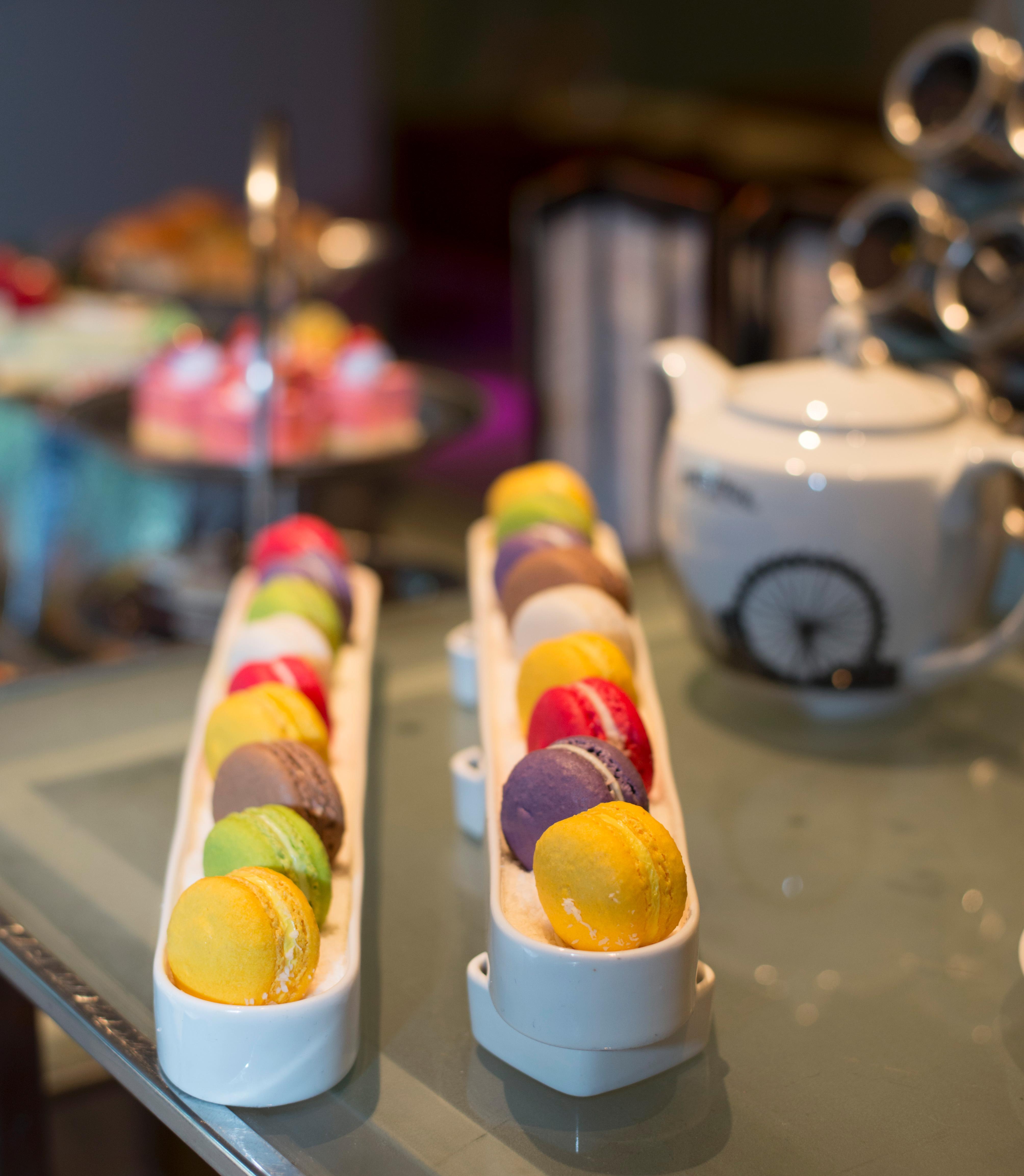 Pathumwan Princess Hotel - Sha Extra Plus Certified Bangkok Exterior foto The photo showcases an elegant display of macarons arranged in two long, narrow trays. The macarons come in a variety of colors, including yellow, green, pink, purple, and orange, suggesting a range of flavors. In the background, there is a white tea