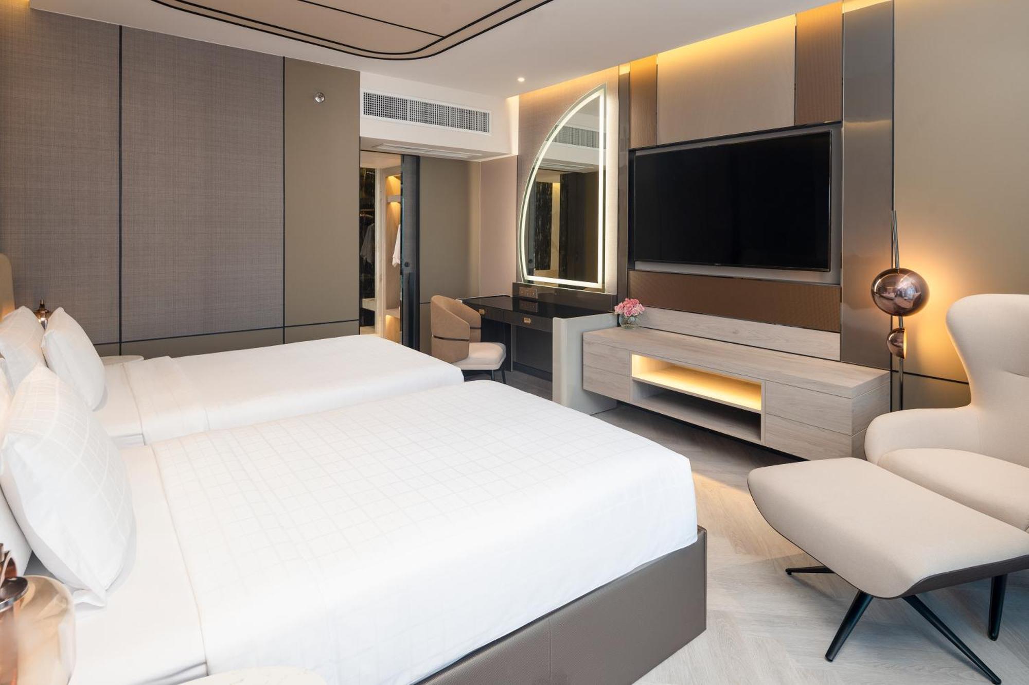 Pathumwan Princess Hotel - Sha Extra Plus Certified Bangkok Exterior foto The photo shows a modern hotel room featuring two beds with white bedding. The room has a sleek design with a combination of neutral colors and stylish lighting. There's a large flat-screen TV mounted on the wall, a work desk with a chair, and a comf