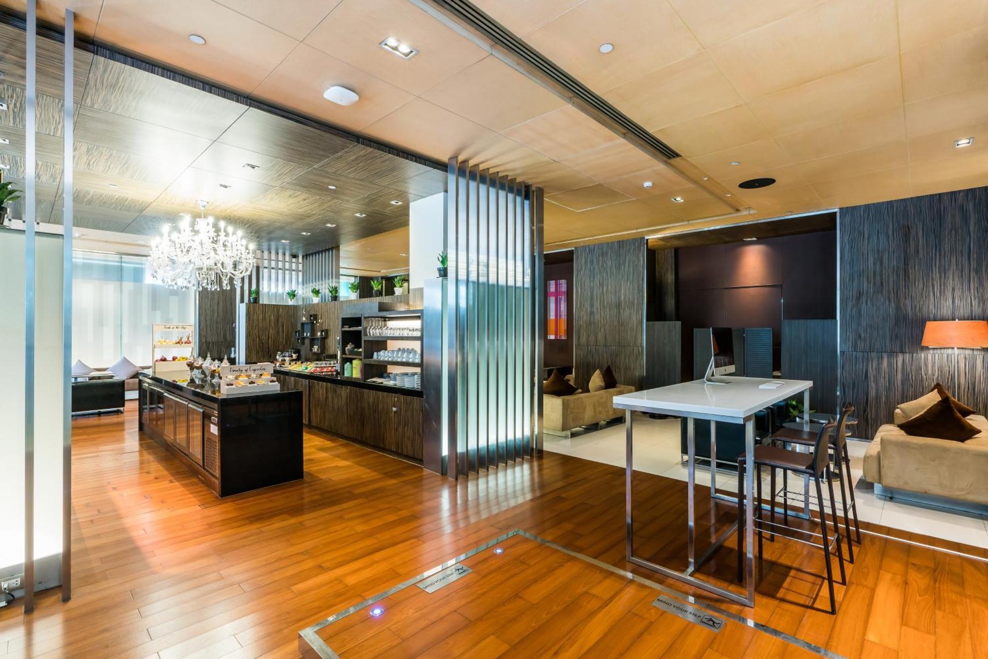 Pathumwan Princess Hotel - Sha Extra Plus Certified Bangkok Zimmer foto The photo shows a modern and stylish interior space, likely a lobby or lounge area. It features elegant wooden flooring and contemporary furnishings. On one side, there is a sleek, dark-colored counter or bar area with various items displayed, possib