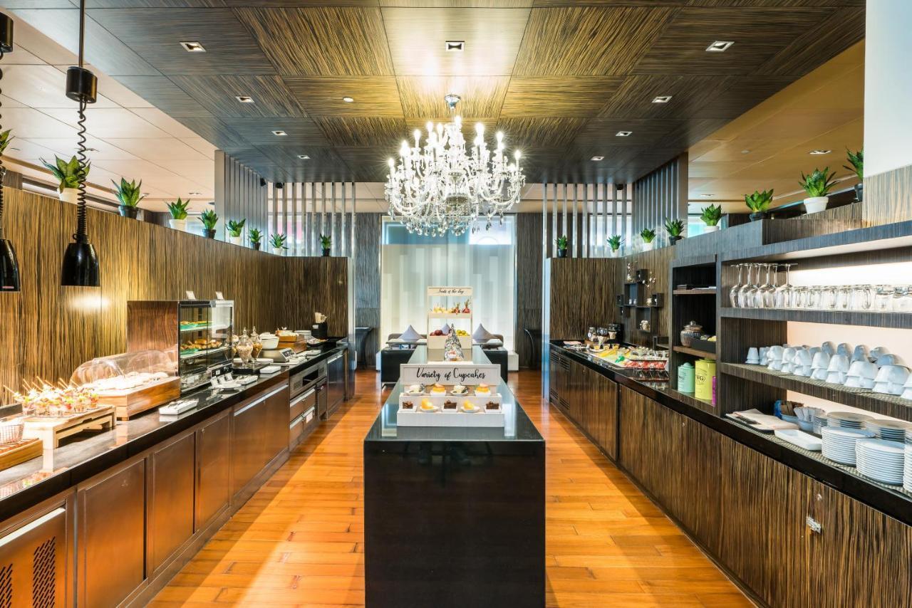 Pathumwan Princess Hotel - Sha Extra Plus Certified Bangkok Exterior foto The photo shows a modern restaurant or buffet area with a stylish interior. The space features wooden walls and flooring, creating a warm ambiance. A large chandelier hangs from the ceiling, adding elegance to the setting. On the right side, there ar