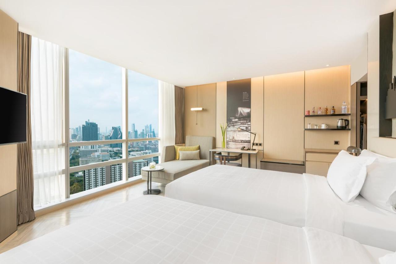 Pathumwan Princess Hotel - Sha Extra Plus Certified Bangkok Exterior foto The photo shows a modern hotel room featuring two beds neatly made with white linens. Large windows allow natural light to flood the space, offering a panoramic view of the city skyline outside. The room is decorated in a contemporary style, with lig